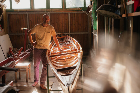 Man working on wooden boat in sunny indoor workshop