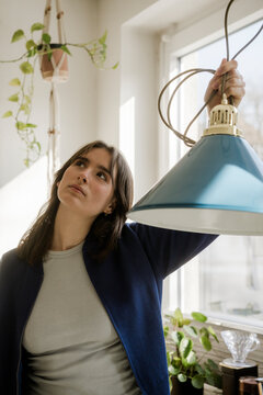 Young woman inspecting a blue lamp for interior design at home