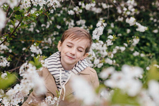 Smiling boy with eyes closed standing among blooming cherry trees outdoors