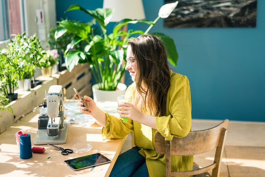 Fashion designer sitting at desk in her studio using smartphone