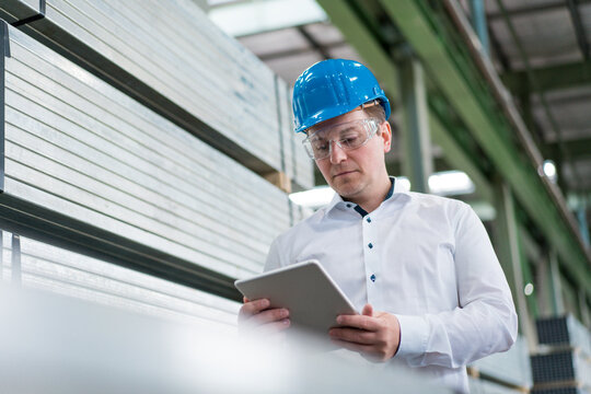 Businessman wearing hard hat and safety goggles in a factory using tablet
