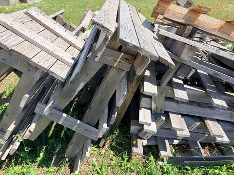 Pile of old weathered wooden planks and dismantled pallets on green grass