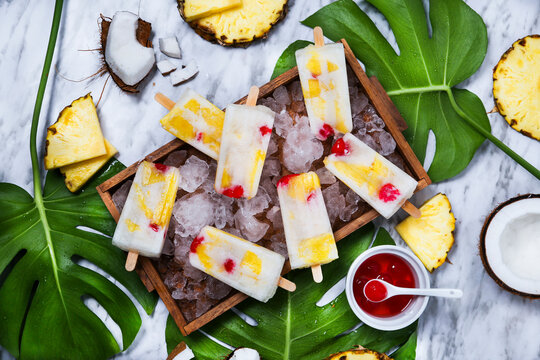 Pina Colada popsicles with candied cherries and pineapple on leaf