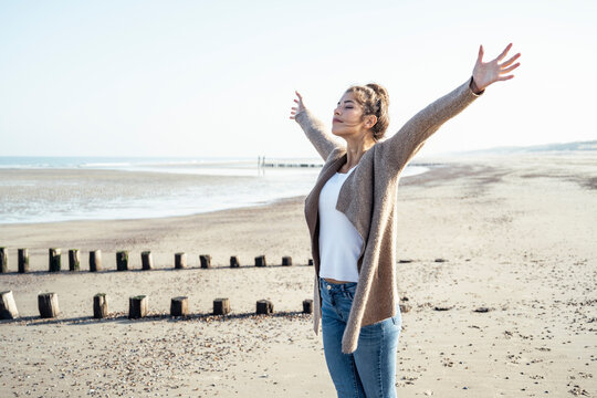 Carefree woman with arms outstretched standing on sand at beach