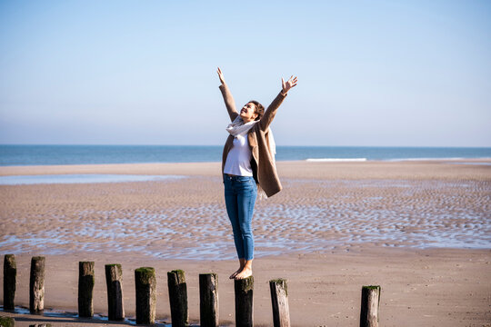 Happy traveler balancing barefoot on beach breakwater in sunlight