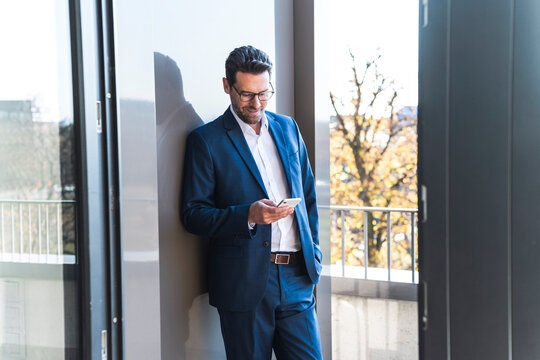 Smiling businessman reading message on smartphone at office balcony