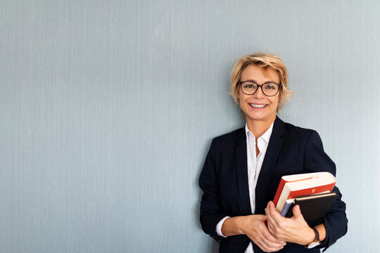 Portrait of mature businesswoman standing at a wall holding stack of books