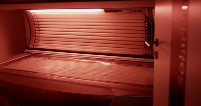 Interior view of a closed tanning bed with illuminated red light lamps inside