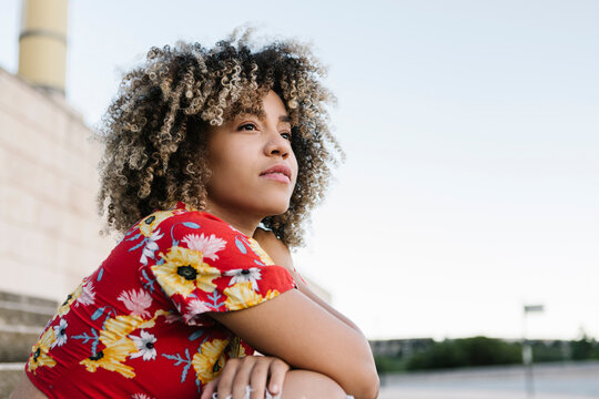 Thoughtful trendy woman sitting against clear sky during sunny day