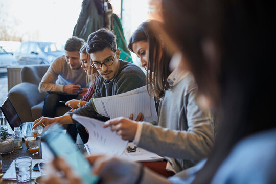 Group of friends sitting together in a cafe with laptop and documents