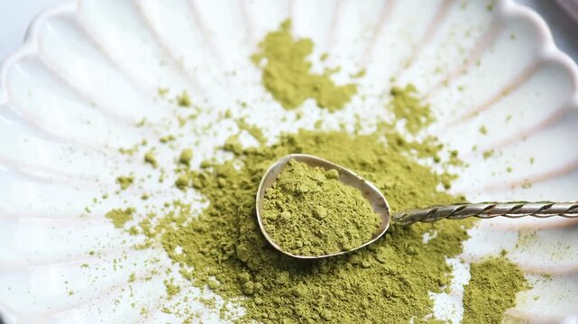 Green tea matcha powder on a spoon over a white plate