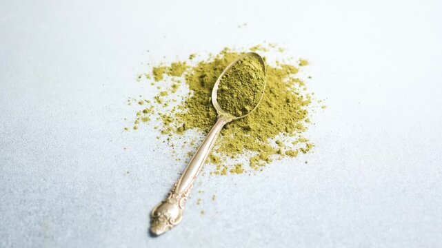 A spoon of matcha powder rests on a textured surface