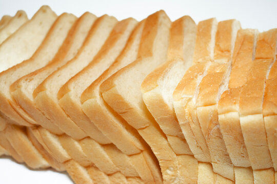 Fresh white sandwich bread slices lined up in a close-range view, highlighting the golden crust and fluffy interior with a repeating pattern.