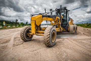 Modern yellow motor grader operating on road construction site