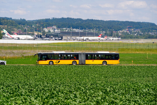 Side view of Swiss Post bus line 510 passing at Swiss Village of R&uuml;mlang with Z&uuml;rich Airport in the background on a sunny summer day. Photo taken June 29th, 2026, Zurich R&uuml;mlang, Switzerland.