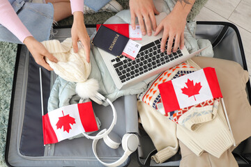 Naklejka premium Young couple of tourists with Canadian flags and laptop packing suitcase at home, top view