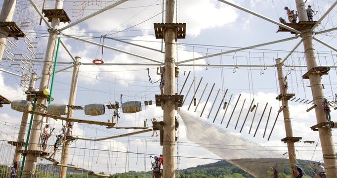 Wide shot of an outdoor high ropes obstacle course with multiple people climbing