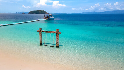 Empty twin wooden swing on Madam beach of Nyaung Oo Phee Island in Myanmar or Burma. Andaman tropical view of turquoise clear water and white sand with tour boat anchoring on a floating dock behind. © zephyr_p