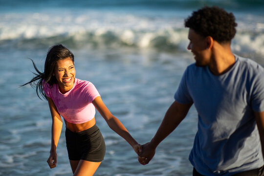 Smiling young woman holding hands with boyfriend at ocean shore