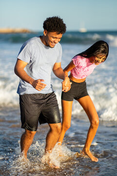 Playful young couple splashing water while running on beach