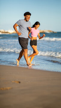 Happy young couple jogging together along sunny beach shoreline