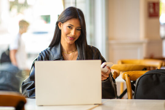 Confident woman working on laptop and smartphone in cafe