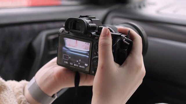 Hands hold camera inside car, focusing on viewfinder. Person captures scenic road ahead. Candid moment of travel photography. Ideal for road trip or travel vlogs. Suitable for travel, adventure