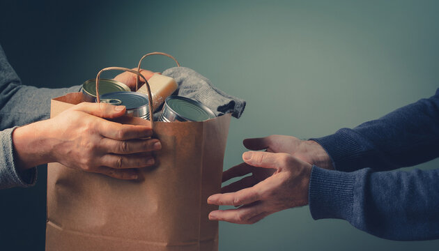 Hands sharing a paper donation bag filled with essential canned food supplies