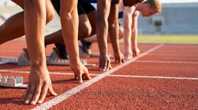 Low-angle view of runners with hands on the starting line in blocks, preparing for a sprint race on a running track