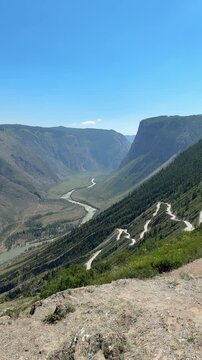 A high-angle view captures the winding Katu Yaryk Pass road and Chulyshman River in Altai, Russia
