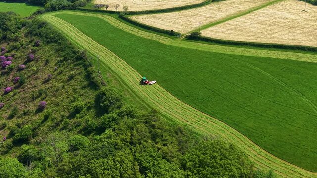 Aerial View of Lush Green Field of Agricultural Tractor mowing green field in English countryside in spring. Agricultural industries, commercial landscaping, rural lifestyle. 4K.