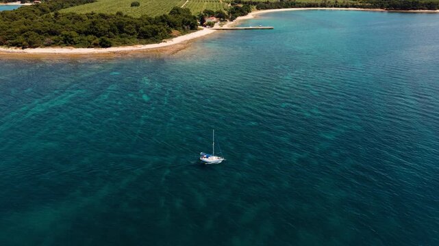 White yacht sailing along the scenic green coastline of Pula. Clear blue Adriatic Sea, aerial view.