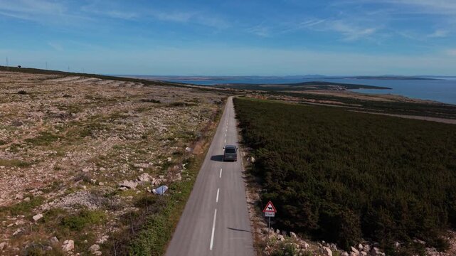 Camper van driving along a lonely coastal road on Pag Island, Croatia. Aerial car following shot