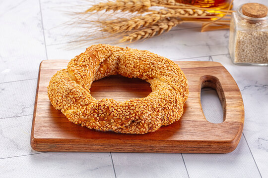 Sesame seed bread ring semit on wooden cutting board with wheat stalks and spice jar