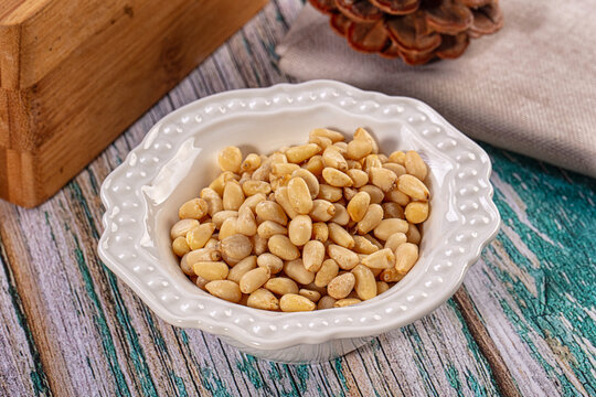 Shelled pine nuts in a white ceramic bowl on a rustic turquoise wooden background