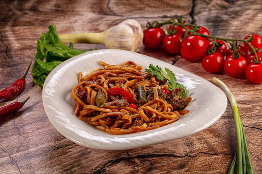 Asian stir fried noodles with beef and vegetables on a rustic wooden table