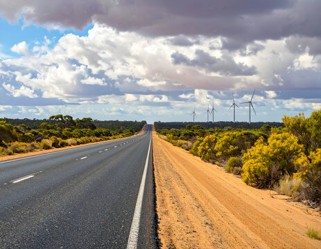 Long Straight Road Through Arid Landscape Towards Wind Turbines Under Dramatic Sky.