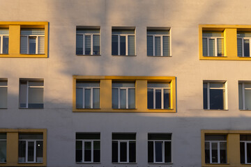 Fototapeta premium Symmetrical facade of a modern residential building featuring yellow framed windows in sunset light to provide a minimalist architectural background with clean lines and urban patterns