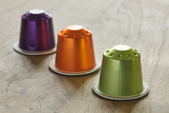 Closeup of three colorful coffee capsules in a row in green, orange and purple on a wooden table..