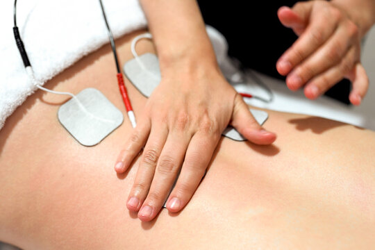 Hands administering electrical muscle stimulation on a bare lower back