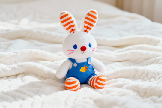 A soft plush rabbit toy with striped ears, blue overalls, and a yellow chick detail, placed on a white textured surface.
