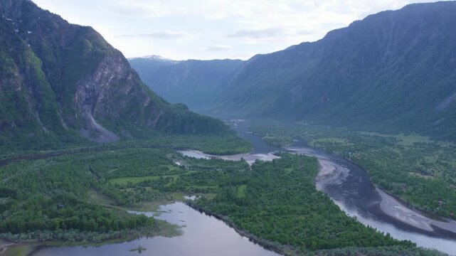 Braided river valley with reflective pools and sandbars beneath steep rocky mountains in broad aerial view, with river, valley, forest, mountain detail, showing braided, sandbar, island, floodplain