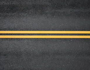 Fototapeta premium A detailed overhead shot showcases a dark asphalt road surface marked with two bright yellow lane dividers, creating a clear visual guide for traffic.