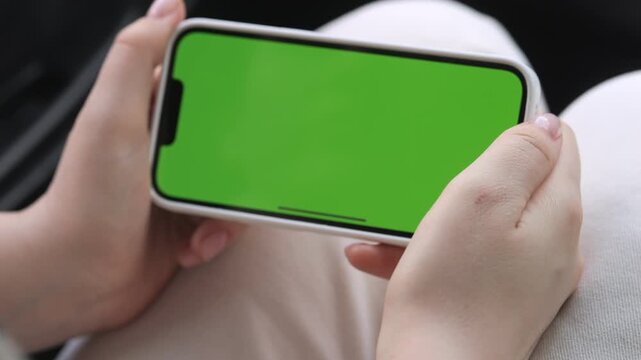 Close-up of hands holding smartphone with green screen. Fingers gently grip device, showing careful handling. Person appears calm and focused on screen. Ideal for app demos, digital ads, or UI mockups