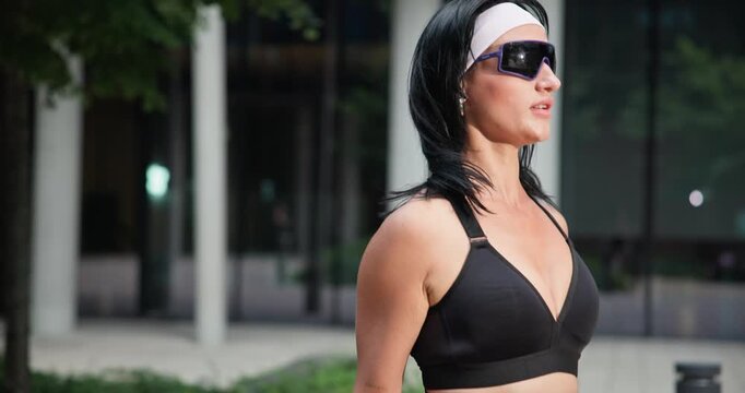 Young beautiful woman athlete in sportswear training and jumping rope in an urban park among high-rise buildings and trees