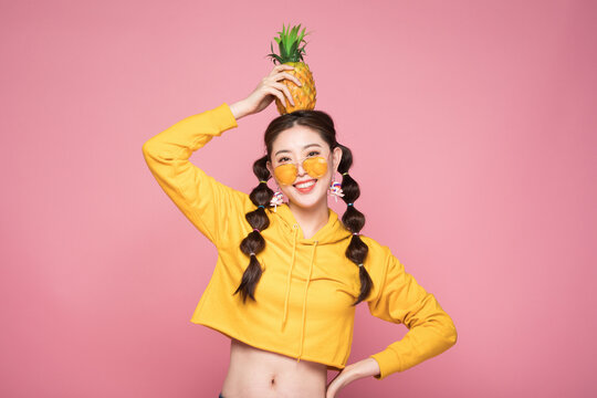 Playful young woman balancing pineapple on her head on pink background