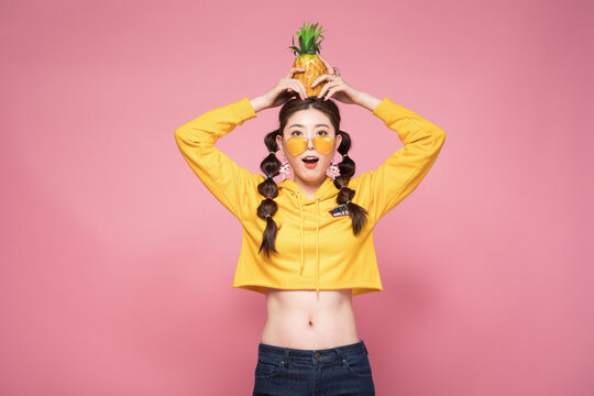 Playful young woman balancing pineapple on head against pink background