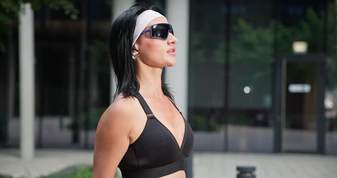 Young beautiful woman athlete in sportswear training and jumping rope in an urban park among high-rise buildings and trees