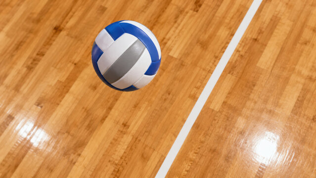 Blue and white volleyball ball bouncing on a wooden gym floor court