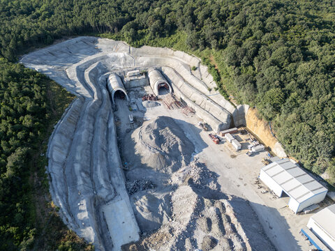 Aerial view of a tunnel construction site with concrete portals, piles of gravel, and heavy machinery surrounded by a dense forest in Istanbul, Istanbul, Turkiye.